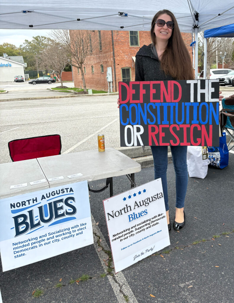Woman holding sign that says "Defend the Constitution or Resign"