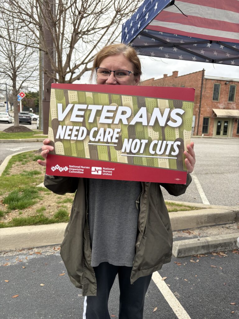 Protestor holding sign that says "Veterans need care, not cuts"